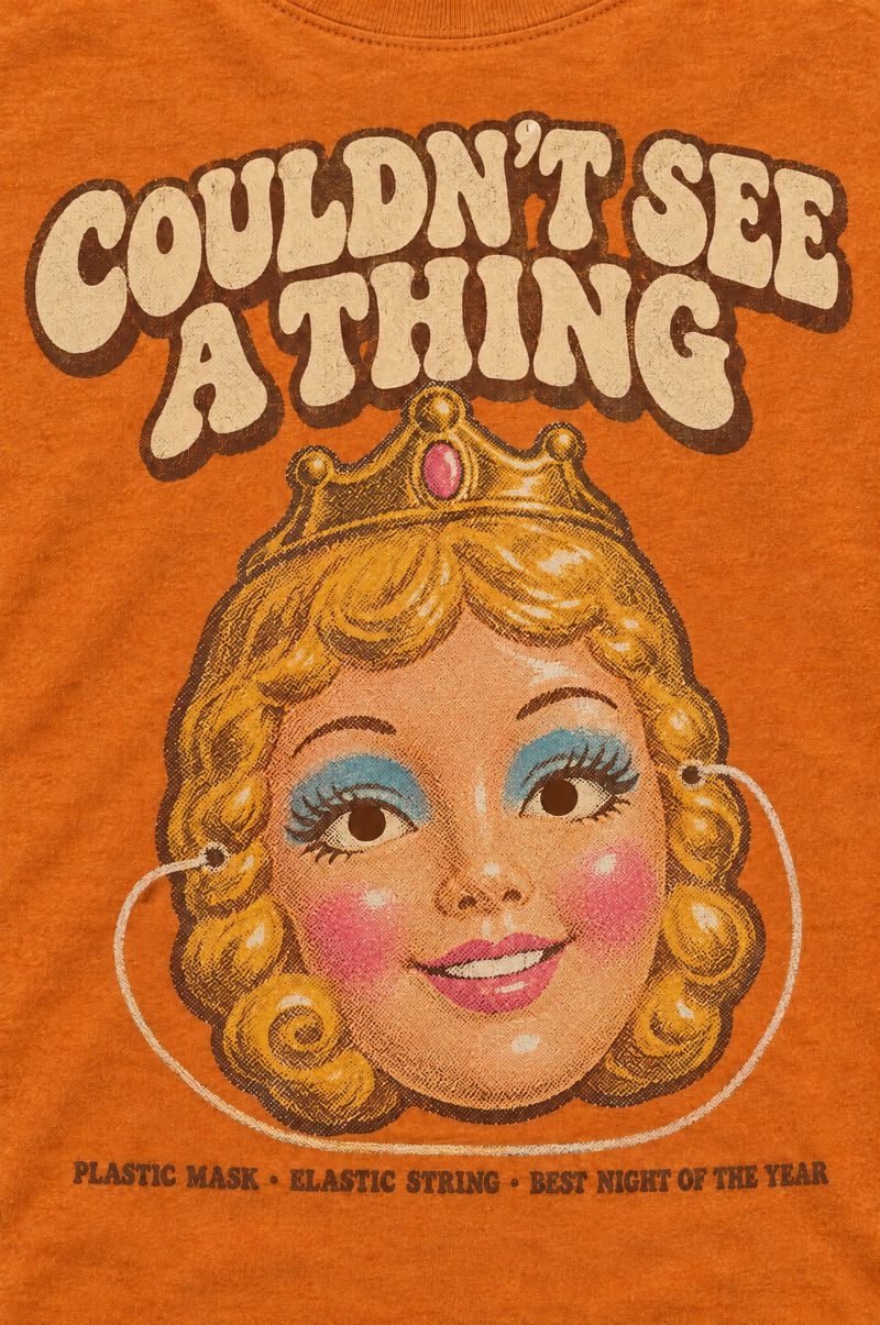 Orange tee printed with a smiling plastic dime-store princess mask with a crown and elastic string, words Couldn’t See a Thing