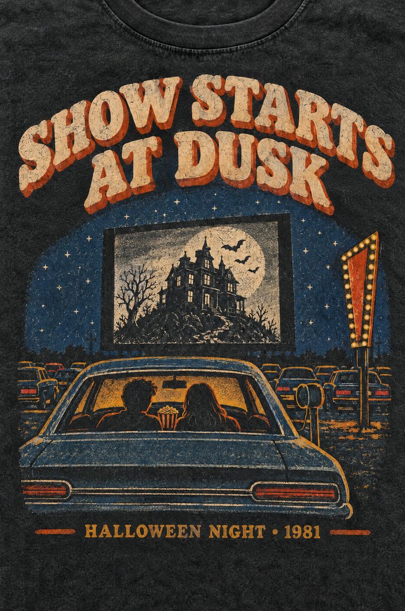 Washed black tee printed with a teenage couple in a car at a drive-in movie theater watching a black-and-white haunted house on the screen, words Show Starts at Dusk, Halloween Night 1981